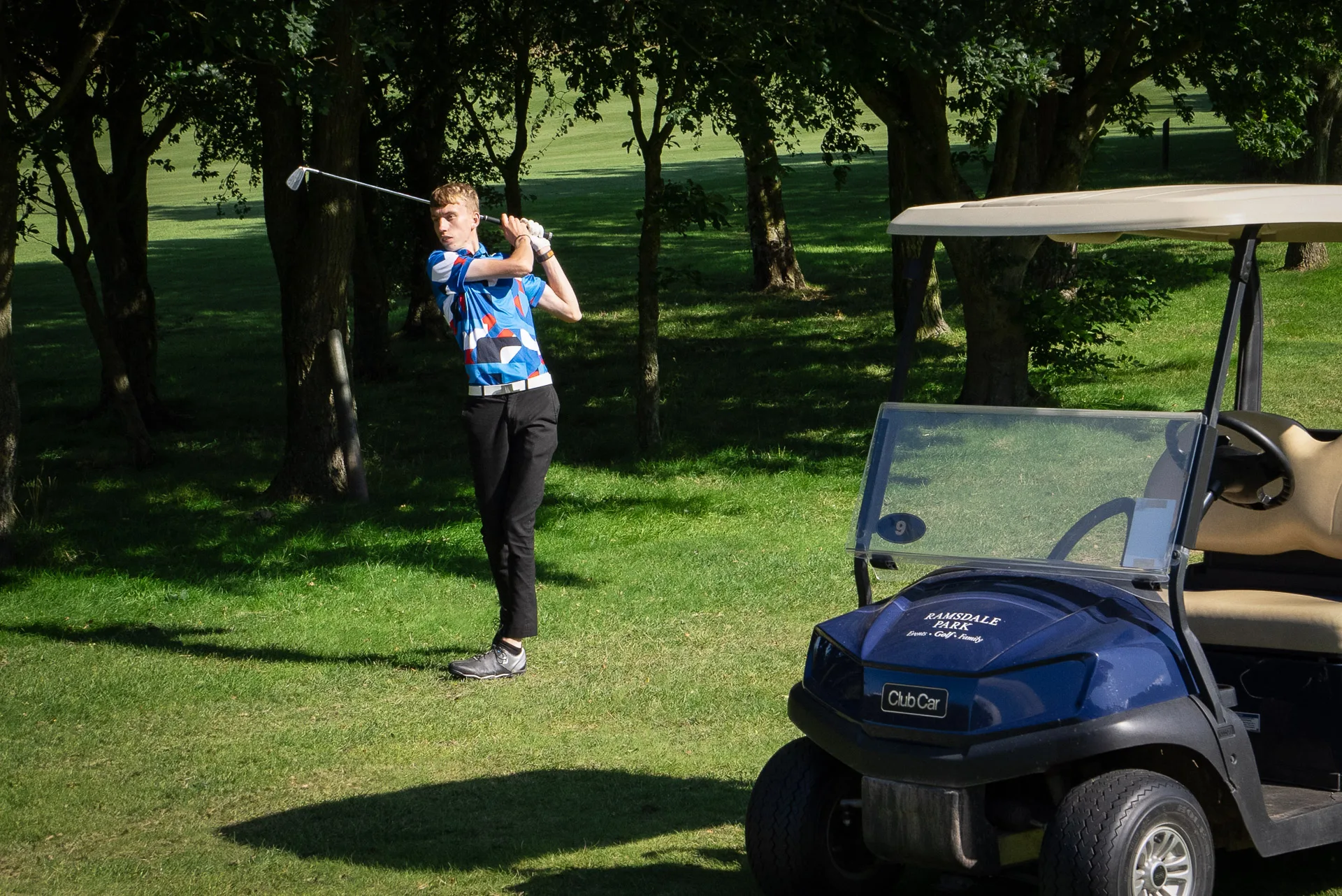 Golfer swinging club by a golf buggy at a golf course in calverton