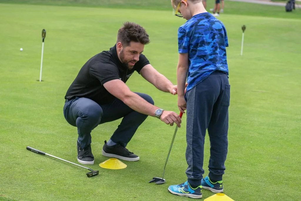 golf coach showing a young boy how to hit a golf ball at a golf lesson in calverton