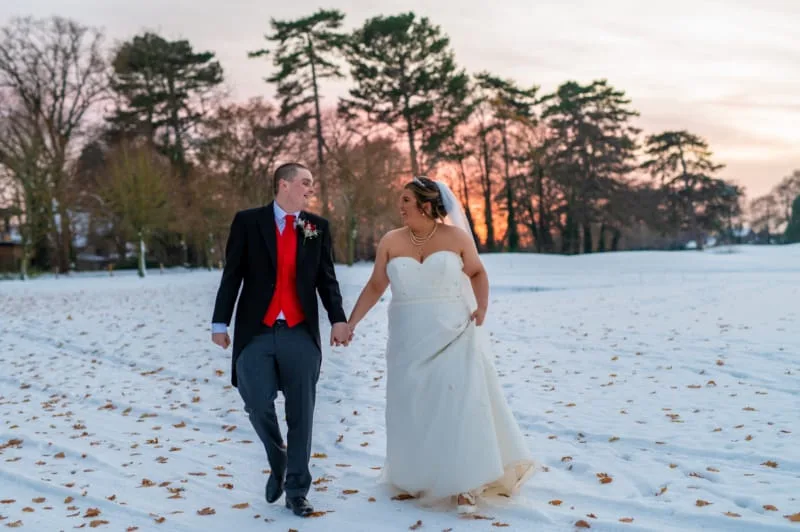 Newly married couple walking down snow-covered fairway after a wedding in nottingham